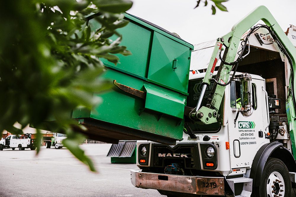Truck picking up dumpster in parking lot