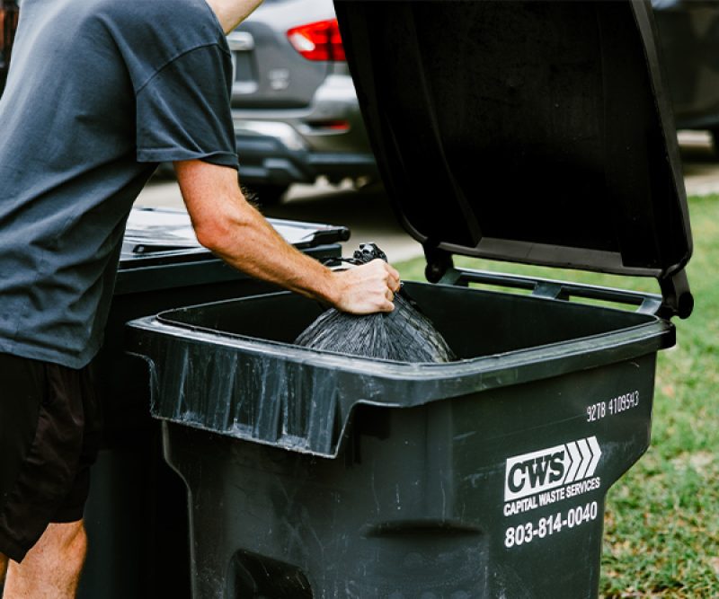 Male resident putting trash bag into residential can for collection