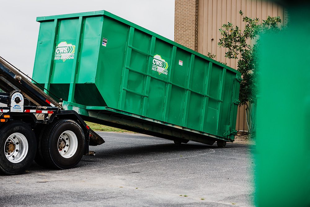 Large dumpster being unloaded from a truck and getting delivered to a business