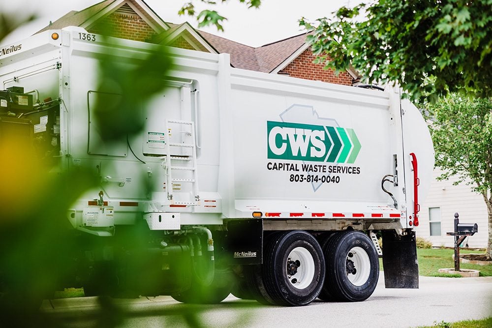 Collection truck on residential street with blurred tree in the foreground